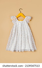 White baby dress with flowers on a hanger on a beige background. ashion kids outfit for summer.
