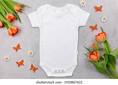 White baby girl or boy bodysuit mockup on the gray concrete background with tulips flowers and summer or spring decoration. Design onesie template, print presentation mock up. Top view. Flat Lay. 