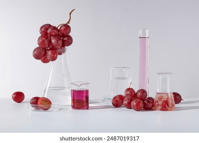 White background featuring several types of lab glassware consist of erlenmeyer flask, beaker, petri dish and measuring cylinder with fresh grape and grape seed extract. Empty space for advertising