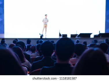 White Background Wall Screen For Presentation. Presenter Presenting On Stage At Conference Auditorium Hall Exhibition. Lecture Speaker. Blurred De-focused Unidentifiable Presenter And Audience.