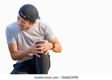 White Background: A Young Asian Male Runner Holding His Knees With His Hands. Sitting On A Park Street From An Exercise Knee Injury: Exercise Injury Concept