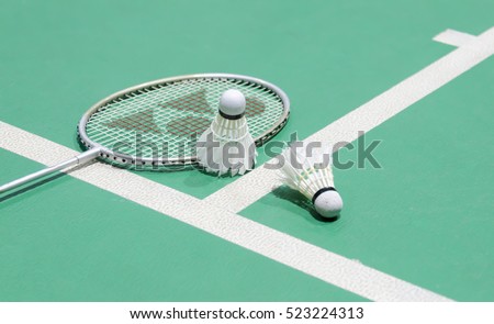 White badminton shuttlecock on a green floor with blurred players in badminton court