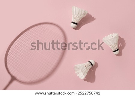 White badminton shuttlecocks and badminton rackets as shadow on pink background. View from above. Creative concept racket sport. Leisure games.