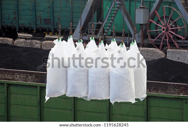 White bags are loading in hold of bulk vessel at\
industrial port. Cargo on the bag loading crane. Loading on railway\
cars, railroad