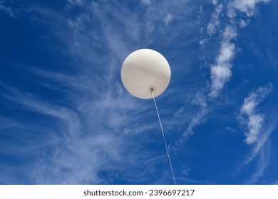 White balloon. A giant inflatable white advertising balloon floats in the sunny blue sky. - Shutterstock ID 2396697217