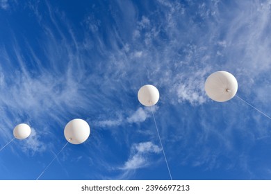 White balloons. A giant inflatable white advertising balloon floats in the sunny blue sky. - Shutterstock ID 2396697213