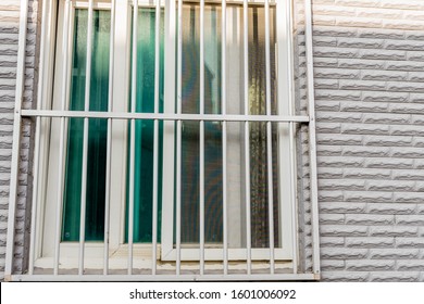 White Bars Installed Over Window On Building With White Brick Exterior.