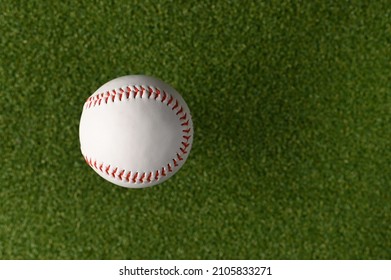 White Baseball Ball On A Green Sports Field. Minimalism. There Are No People In The Photo. Abstraction. Professional And Amateur Sports, Sports Games, Outdoor Activities, Training.