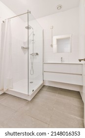 White Bathroom. There Are Large White Tile Wall And Floor.There Have Glass Partition For Shower.Natural Light Transmitted Through The Room