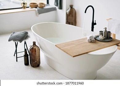White bathtub fills with foam water in a modern apartment with stylish loft-style interior design, home decor. Spa concept, relaxation. Soft selective focus. - Shutterstock ID 1877011960