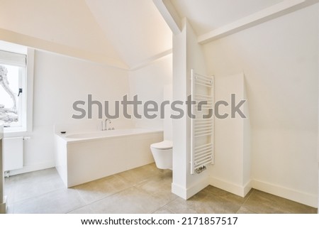 White bathtub with metal faucet next to window and hanging toilet in modern minimalist style bathroom in apartment