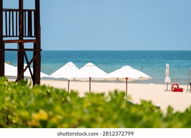 White beach umbrellas on bright Phu Quoc sand with calm blue sea and lifeguard tower