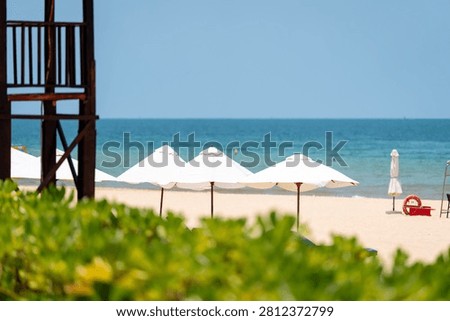 White beach umbrellas on bright Phu Quoc sand with calm blue sea and lifeguard tower
