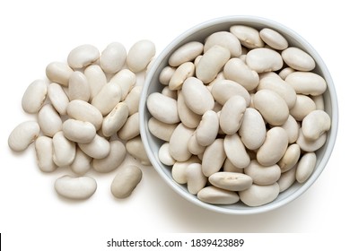 White beans in a white ceramic bowl next to a pile of white beans isolated on white. Top view.
