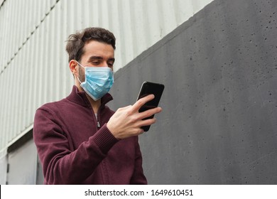 White bearded adult man using smartphone while wearing surgical mask on an industrial wall. Health, epidemics, social media, communication and lifestyle stills with copy space. - Powered by Shutterstock