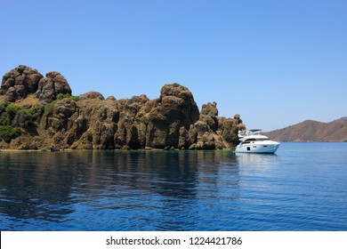 White beautiful yacht is near rocky sea coast at sunny summer day