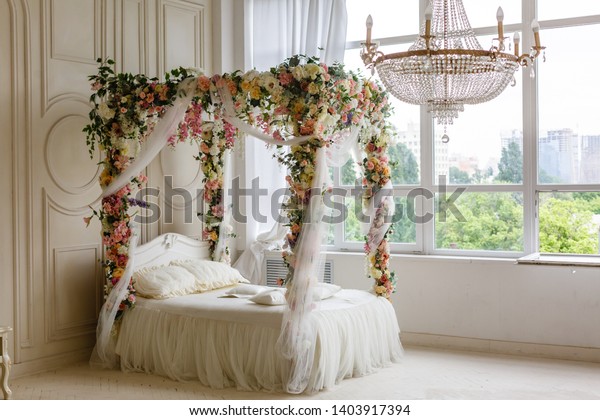 white\
bed. white bed in a classic style with a garland of leaves and\
flowers. the spring location. decorated in a spring decor. the\
white four-poster bed is decorated with\
flowers