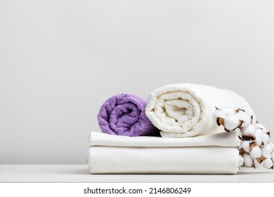 White Bed Linen, Sheets And Terry Towels With A Cotton Branch On A Light Gray Table