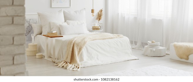 White bedroom interior with windows, gold accessories and white bedsheets on king-size bed