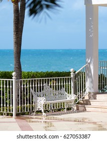 White Bench On The Beach Next To A Palm Tree. Turquoise Water Of The Caribbean Sea In The Background. Holiday In The Paradise. Vacation Concept Image. Vertical Wallpaper.