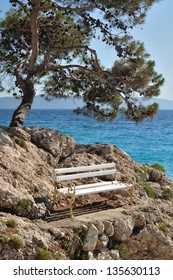White bench on stones under the tree, with sea in background. Podgora, Croatia