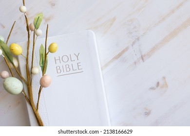 White bible and decorative branch with easter eggs on a white wood background with copy space