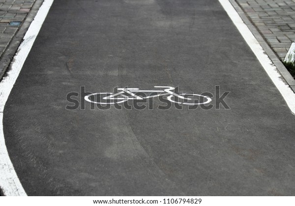White bicycle sign with arrow on the asphalt,\
bike road sign on the street, bicycle lane sign on street, gray\
background