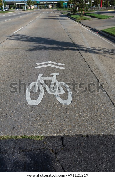 White bicycle sign on asphalt bike lane on city\
street. Concept background for Air Pollution Reduce and Cycling\
Health Benefits.