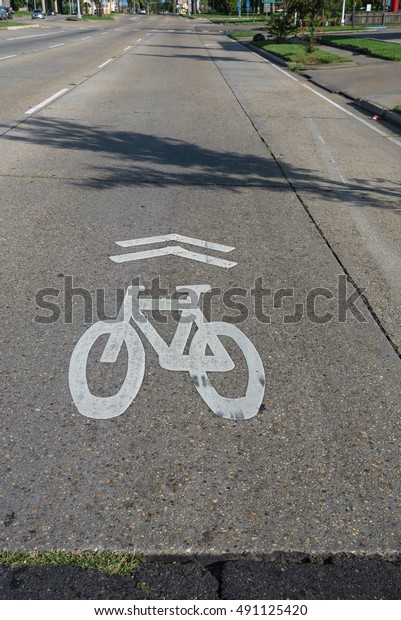 White bicycle sign on asphalt bike lane on city\
street. Concept background for Air Pollution Reduce and Cycling\
Health Benefits.