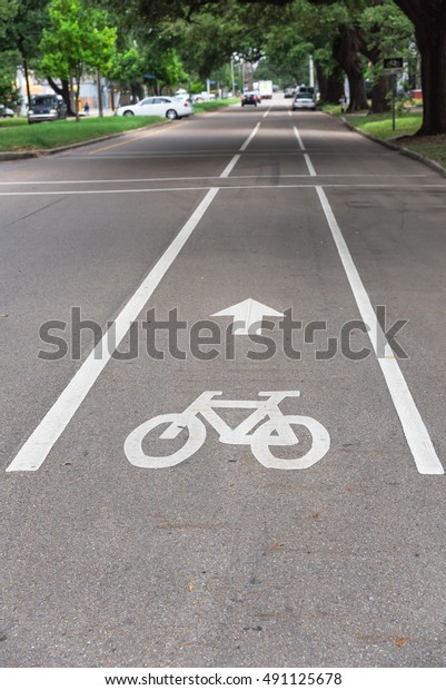 White bicycle sign on asphalt bike lane\
on city street with cars in background. Concept background for Air\
Pollution Reduce and Cycling Health\
Benefits.