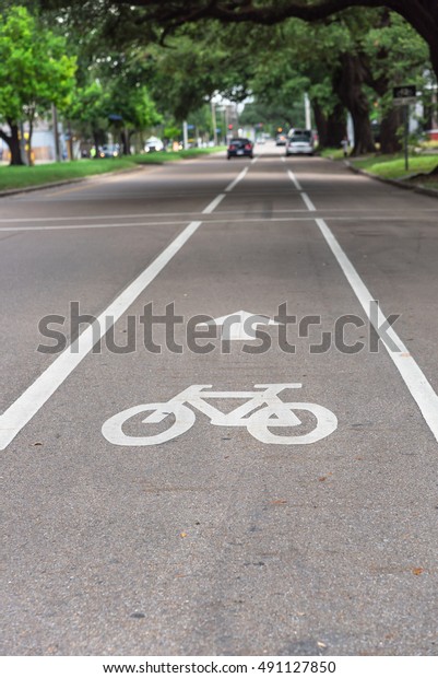 White bicycle sign on asphalt bike lane\
on city street with cars in background. Concept background for Air\
Pollution Reduce and Cycling Health\
Benefits.