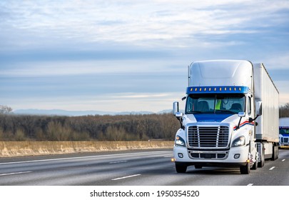 White Big Rig Industrial Semi Truck Transporting Commercial Cargo In Dry Van Semi Trailers Driving In Front Of Truck Convoy On The Wide Multiline Elevated Interstate Highway Road