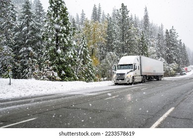 White big rig industrial semi truck with grille guard transporting cargo in dry van semi trailer standing on road shoulder of a winter highway during a snow storm near Shasta Lake in California