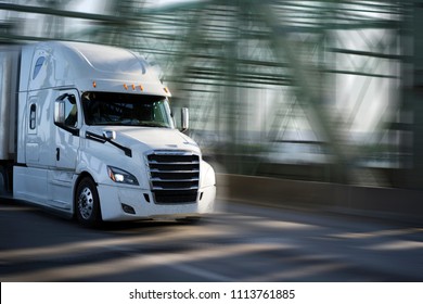 White Big Rig Semi Truck With Chrome Grille Transporting Goods In Semi Trailer Driving On Arched Truss Interstate Columbia River Draw Bridge For Delivery Of Commercial Cargo To Destination Warehouse