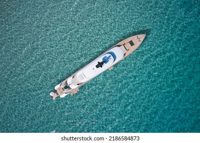 White Big Yacht For A Billionaire Anchored Aerial View. Mega Yacht On Blue Water Aerial View. Modern Big White Yacht On Transparent Water Top View.