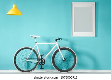 White bike against blue wall with grey poster in living room interior with yellow lamp