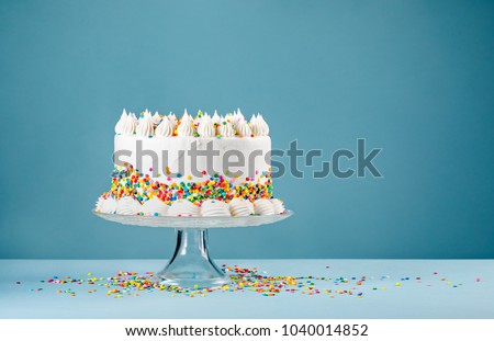White Birthday cake with colorful Sprinkles over a blue background.
