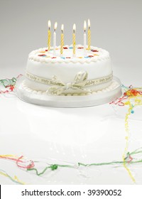 A White Birthday Cake With Light Candles And Streamers