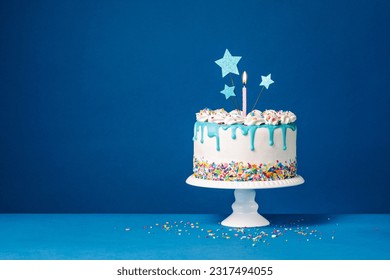 Torta de goteo de cumpleaños blanco con ganache de té, estrellas y divertidas velas sobre fondo azul oscuro