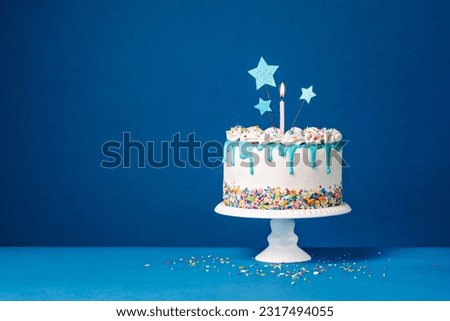 White birthday drip cake with teal ganache, star toppers and fun candles over dark blue background