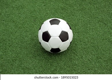 White And Black Ball For Playing Soccer Lays On The Sport Playground On The Green Synthetic Grass Front View Close Up View