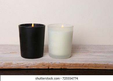 White and black candles. Two burning candles on wooden table against white wall.