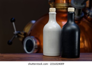 White And Black Ceramic Gin Bottles On A Wooden Counter In Front Of The Copper Still Of A Gin Distillery. Copy Space For Your Design Or Product. Web Banner.