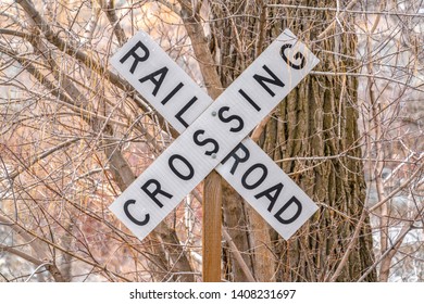 White and black Railroad Crossing sign with leafless trees in the background - Powered by Shutterstock