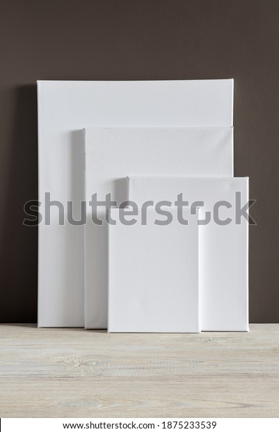 White blank canvases of various sizes stand\
against a dark wall. Mockup. Materials for painting with oil paints\
and acrylics. Close-up\
photo.