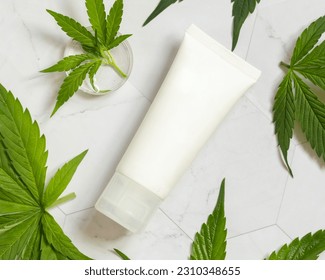 White blank Cream tube near green cannabis sativa leaves on a marble table, top view. Cosmetic Mockup, Copy space. Organic skincare beauty product. Eco friendly body or hand cream with hemp - Shutterstock ID 2310348655