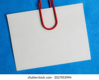 White Blank Note Pinned To A Blue Notice Board With A Paper Clip.