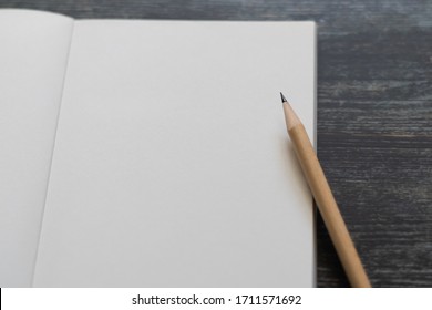 White blank notebook or plain notepd or diary or journal for writing text and message with pencil on old wood table or desk as background with copy space. Still lifestyle photo concept.