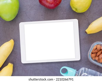 White Blank Screen Tablet And Various Fruits, Water Bottles, And Almonds In A Glass Cup On Grey Background. The Concept Of Health And Design Of Healthy Products. Top View Flat Lay Mockup Screen
