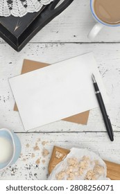 White, blank sheet with space to write down, for example, a recipe for a dish, a cake, or bread. How to prepare the tasty meal. A piece of paper lies on white, wooden boards, surrounded by kitchen items, black pen, brown tray, crocheted doily, cup of coffee with milk, crumbled yeast, milk in small, blue jug and a cutting board. Part of a larger series concerning the local taste. Regional food.